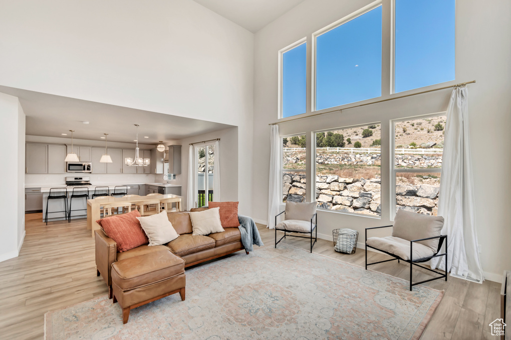 Living area featuring light wood-style flooring, a towering ceiling, a chandelier, and baseboards