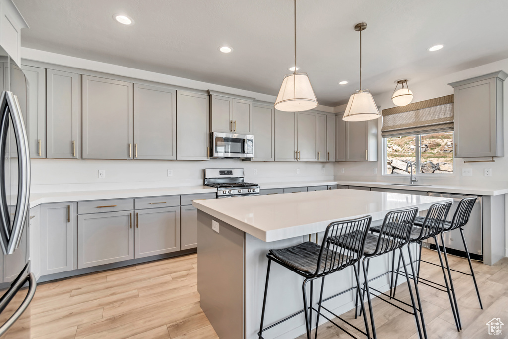 Kitchen featuring gray cabinetry, appliances with stainless steel finishes, a sink, a kitchen island, and a kitchen bar