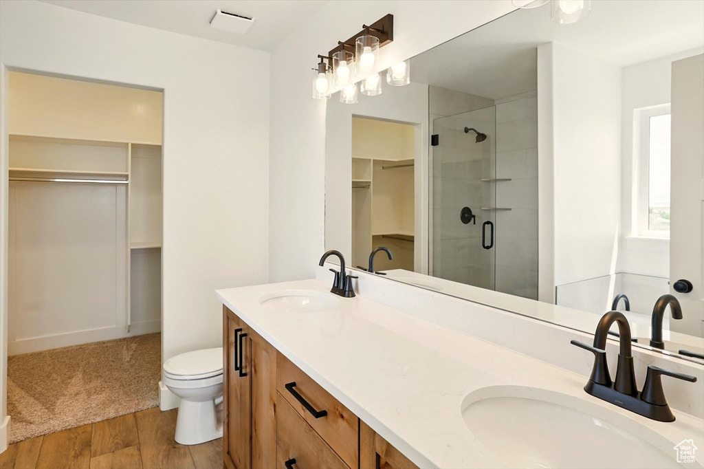 Full bath featuring a spacious closet, a shower stall, double vanity, and wood finished floors