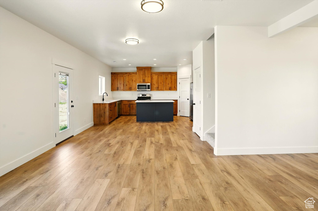 Kitchen featuring appliances with stainless steel finishes, light countertops, brown cabinets, light wood-type flooring, and recessed lighting