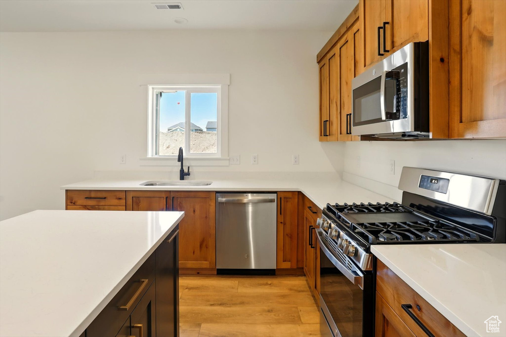 Kitchen with appliances with stainless steel finishes, brown cabinetry, light wood-style flooring, and light countertops