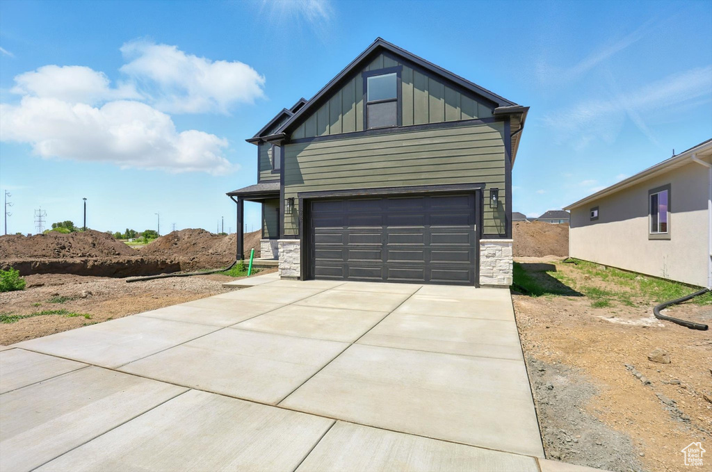 View of front of home featuring board and batten siding, stone siding, driveway, and a garage