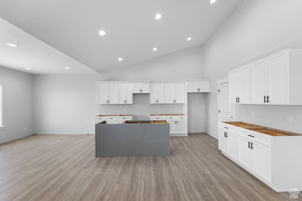 Kitchen featuring a kitchen island, light wood-style flooring, recessed lighting, white cabinetry, and high vaulted ceiling