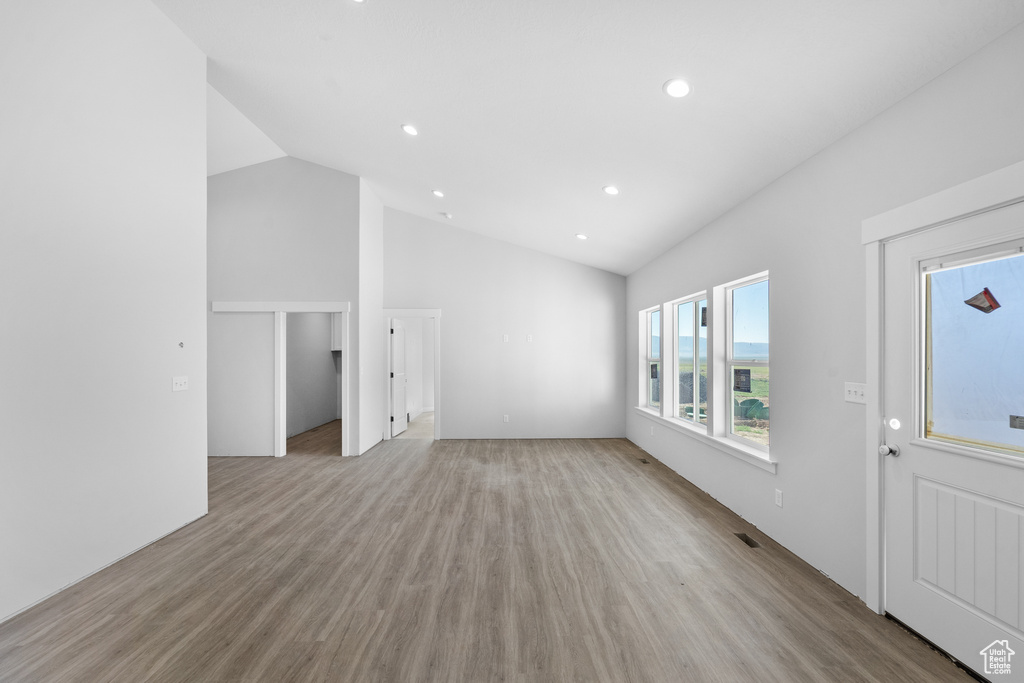 Unfurnished living room featuring vaulted ceiling, light wood-style flooring, and recessed lighting