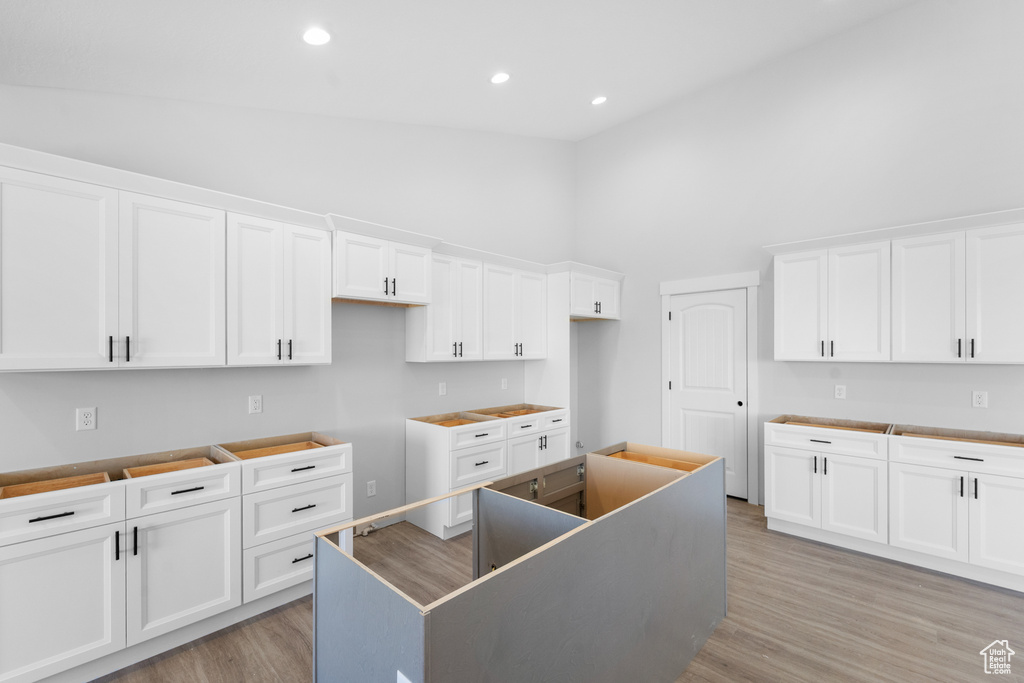 Kitchen with high vaulted ceiling, light wood finished floors, white cabinets, recessed lighting, and a kitchen island