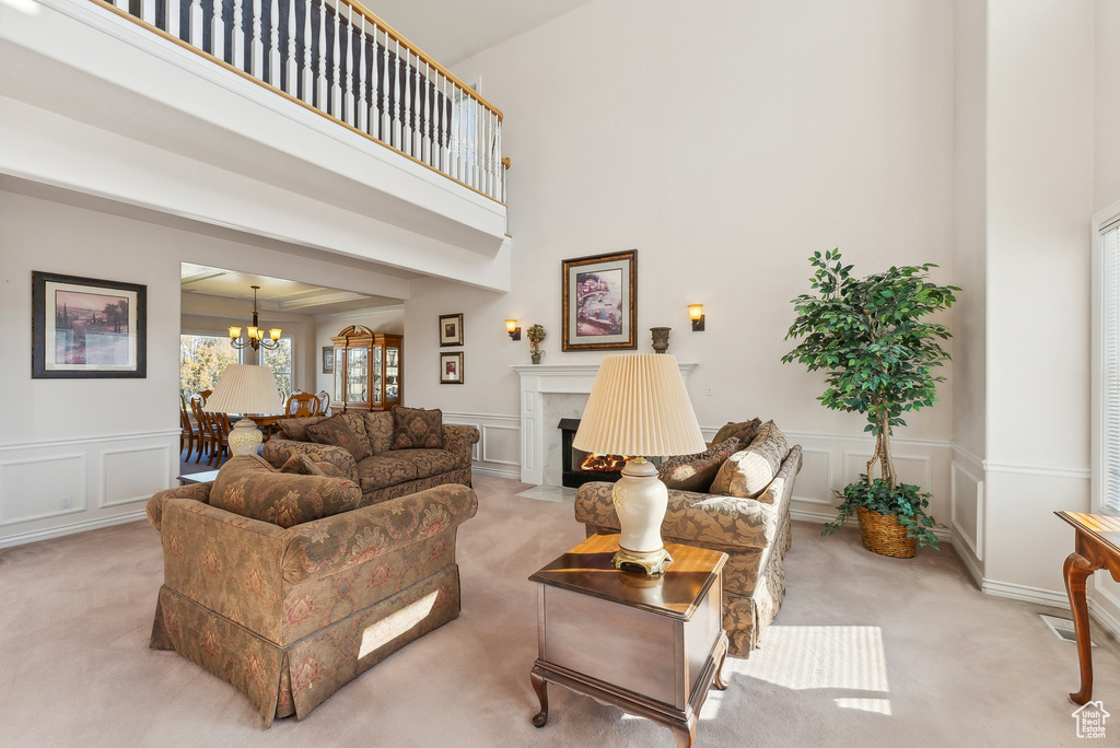 Living area with light carpet, a decorative wall, a chandelier, a high end fireplace, and wainscoting