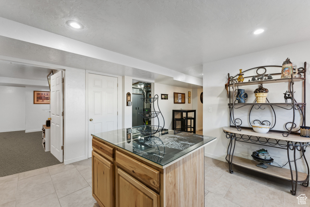 Kitchen with dark countertops, a center island, light tile patterned flooring, recessed lighting, and light carpet