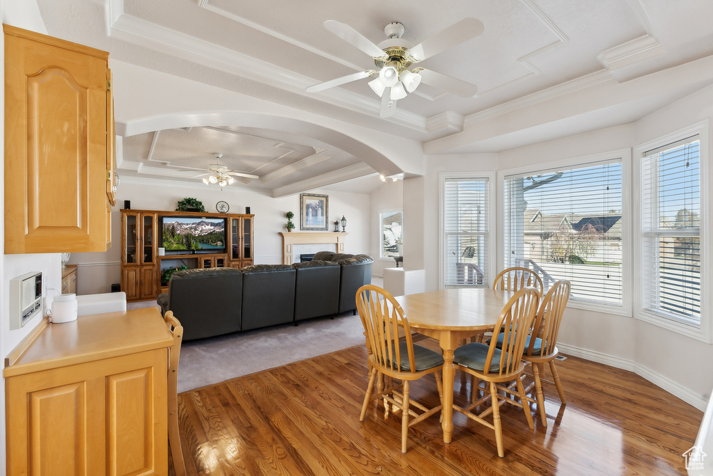 Dining area with a fireplace, ceiling fan, arched walkways, a raised ceiling, and light wood-style floors