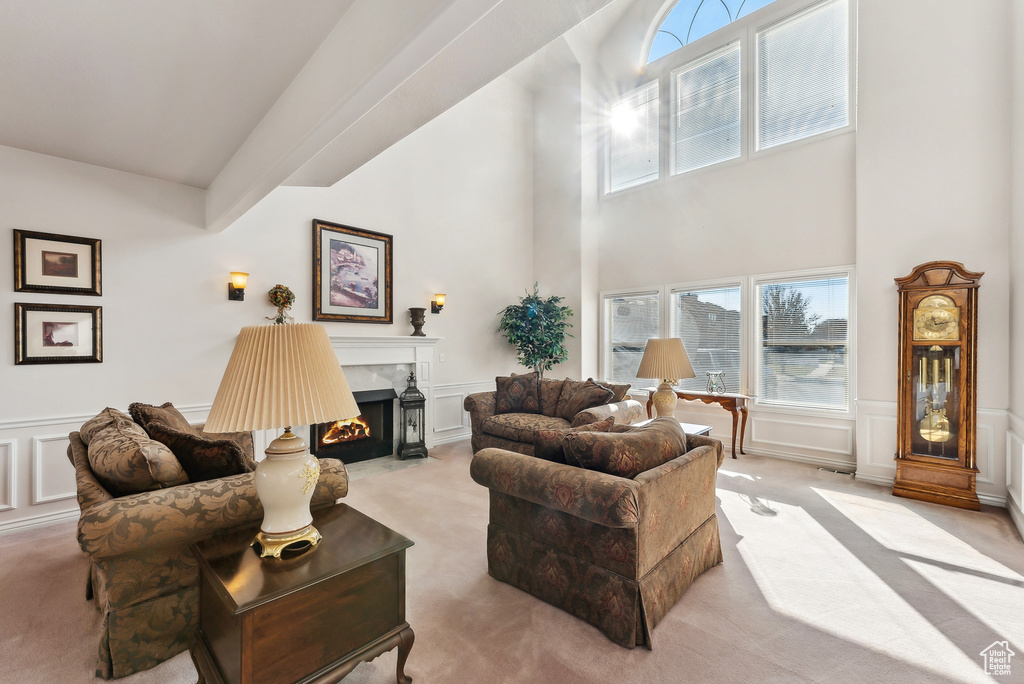 Living room featuring a decorative wall, light colored carpet, a wainscoted wall, a premium fireplace, and a high ceiling