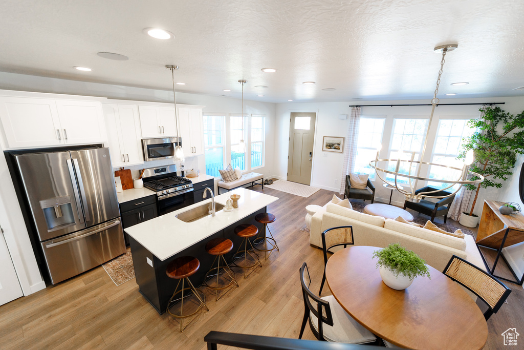 Kitchen with appliances with stainless steel finishes, a kitchen breakfast bar, a center island with sink, light countertops, and light wood-style floors