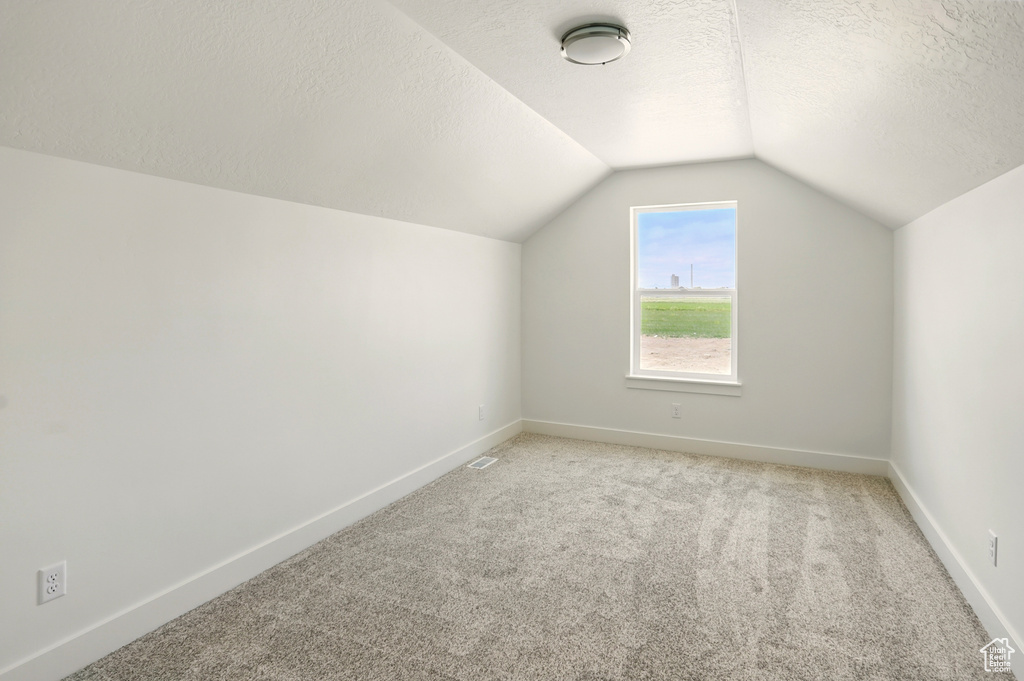 Bonus room with vaulted ceiling, light colored carpet, and a textured ceiling
