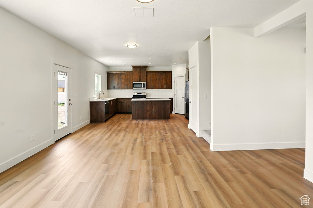 Kitchen with appliances with stainless steel finishes, dark brown cabinetry, light countertops, open floor plan, and light wood-type flooring