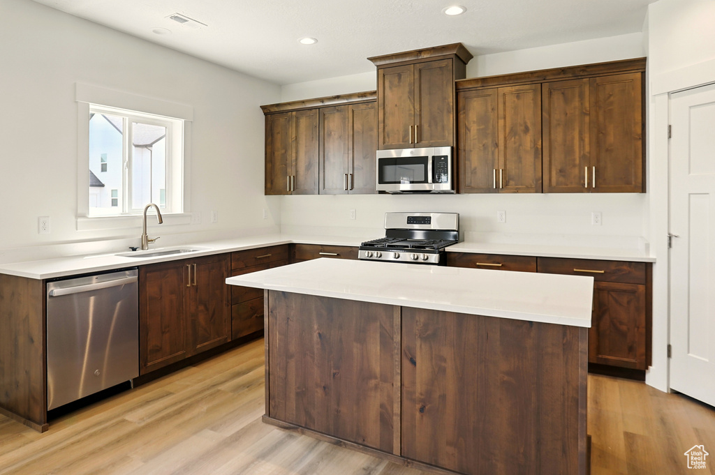 Kitchen featuring appliances with stainless steel finishes, light wood-type flooring, a kitchen island, light countertops, and recessed lighting