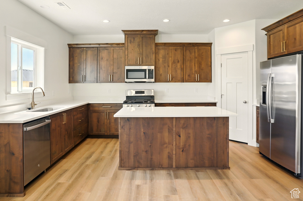 Kitchen with stainless steel appliances, light wood finished floors, a center island, light countertops, and recessed lighting
