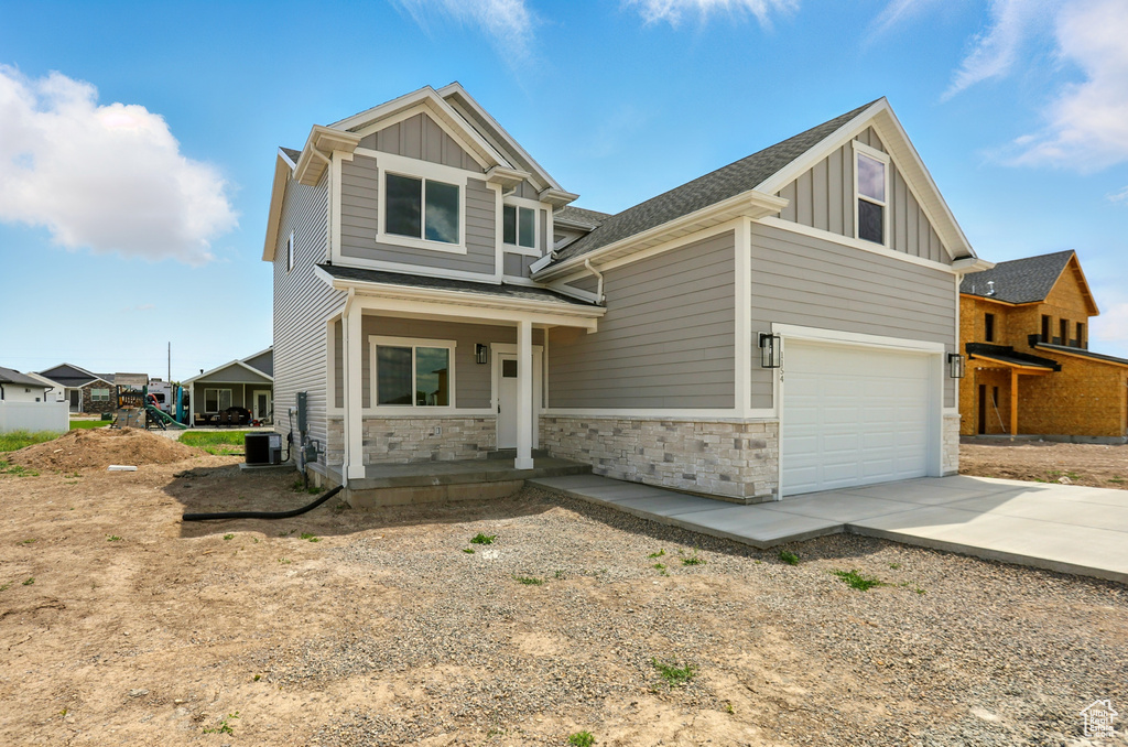 Craftsman-style home featuring board and batten siding, covered porch, concrete driveway, an attached garage, and stone siding