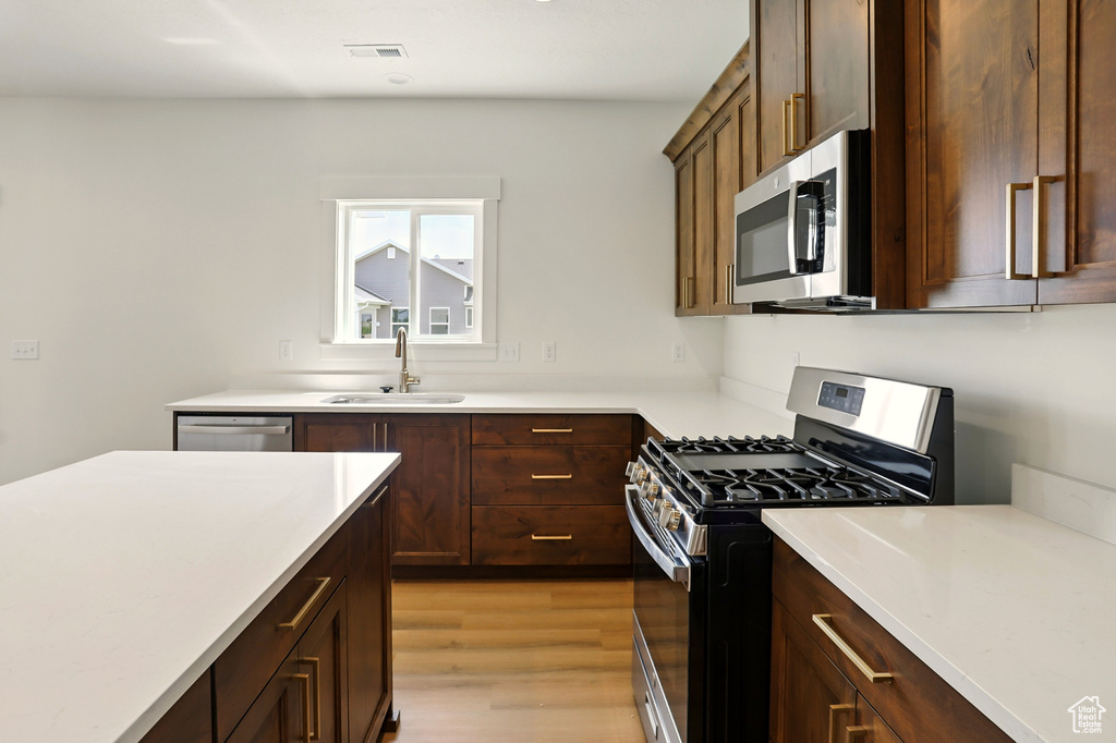 Kitchen with stainless steel appliances, light countertops, light wood-type flooring, and dark brown cabinets