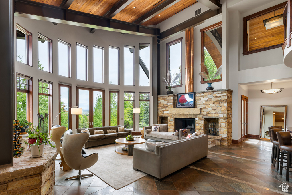 Living room featuring a towering ceiling, healthy amount of natural light, wood ceiling with exposed beams, a fireplace, and baseboards