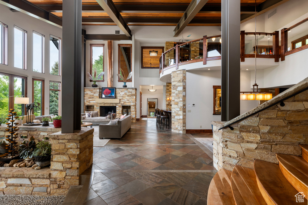 Living room featuring a high ceiling, stone tile flooring, a stone fireplace, ornate columns, and beam ceiling