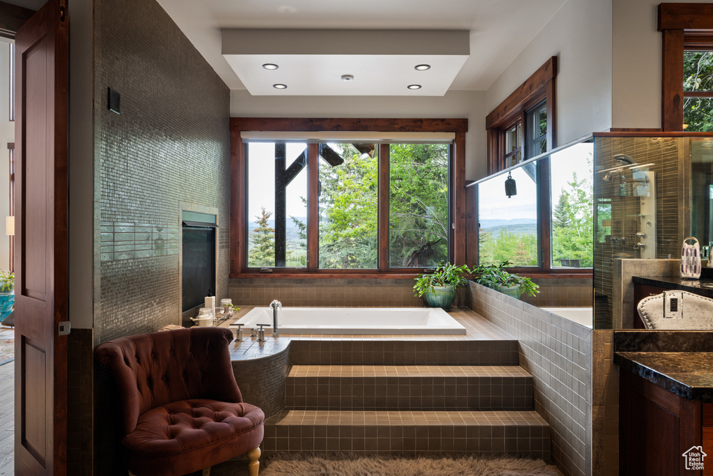Full bath with vanity, a bath, plenty of natural light, a glass covered fireplace, and recessed lighting
