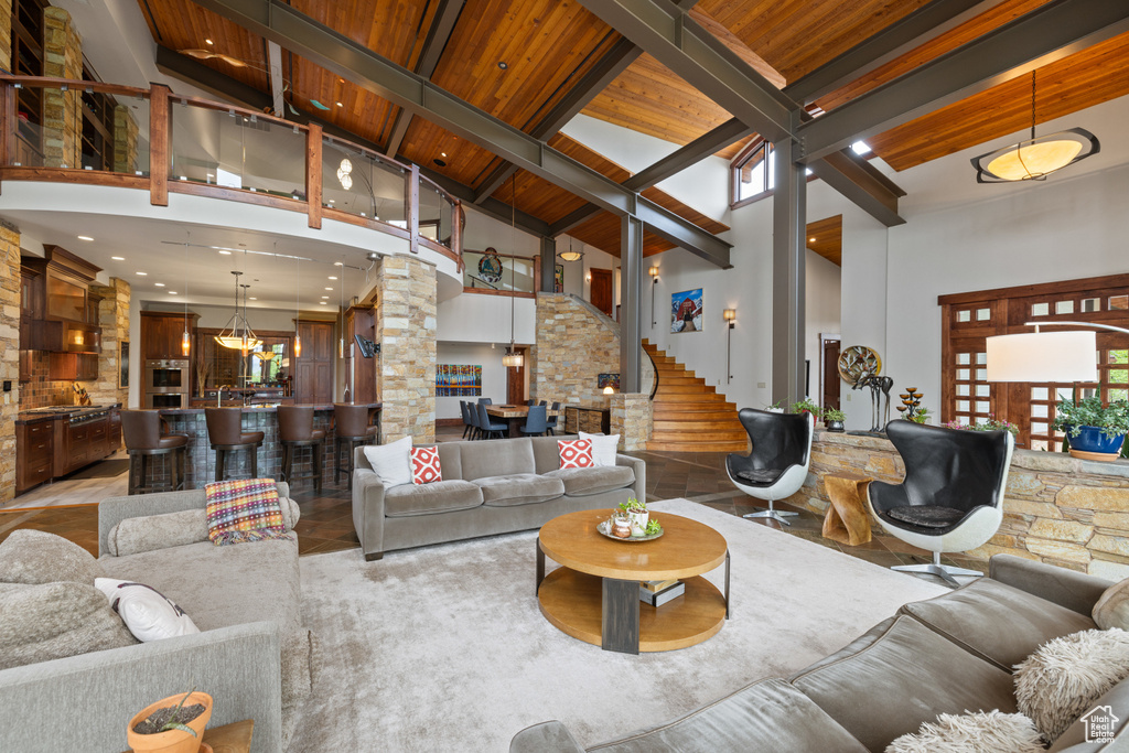Living room featuring high vaulted ceiling, ornate columns, wooden ceiling with exposed beams, and stairway