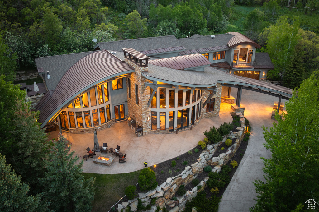 Rear view of house featuring a fire pit, a patio area, a standing seam roof, and stone siding