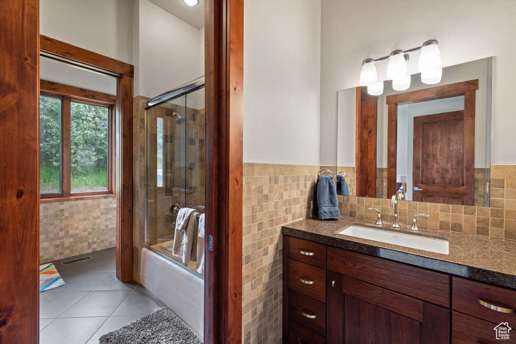 Bathroom with tile walls, vanity, bath / shower combo with glass door, tile patterned floors, and wainscoting