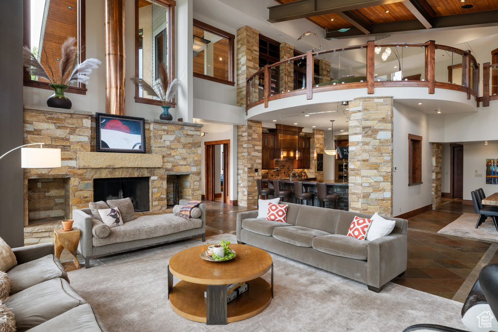 Living room with a high ceiling, wooden ceiling with exposed beams, a stone fireplace, and baseboards