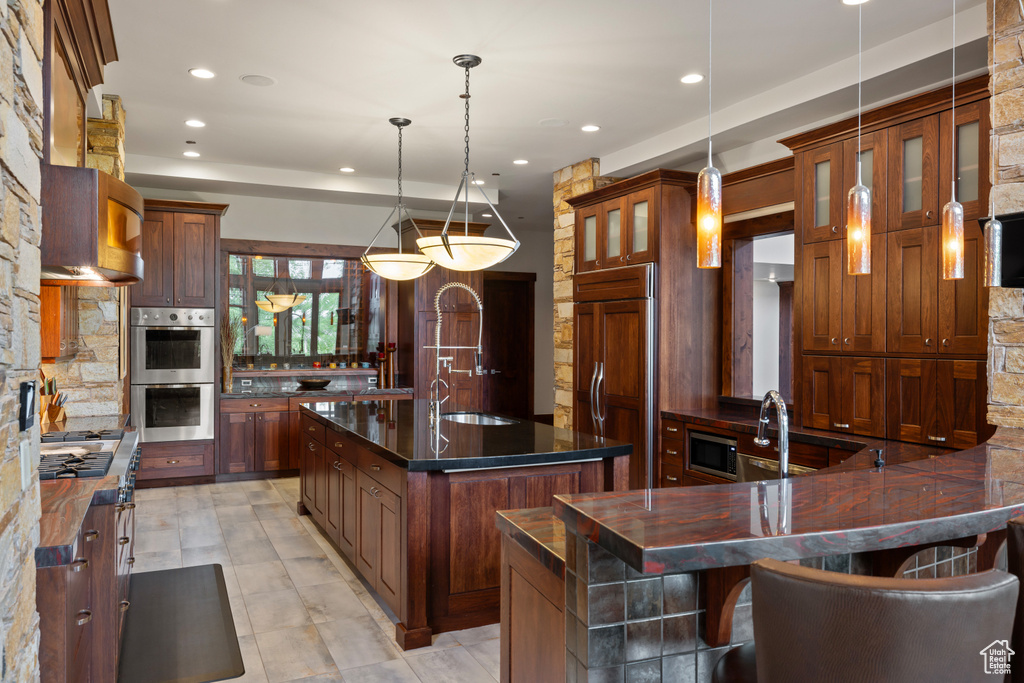 Kitchen featuring built in appliances, a sink, a center island with sink, glass insert cabinets, and recessed lighting