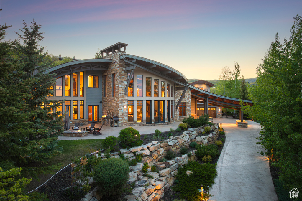 Back of property at dusk featuring stone siding and a patio
