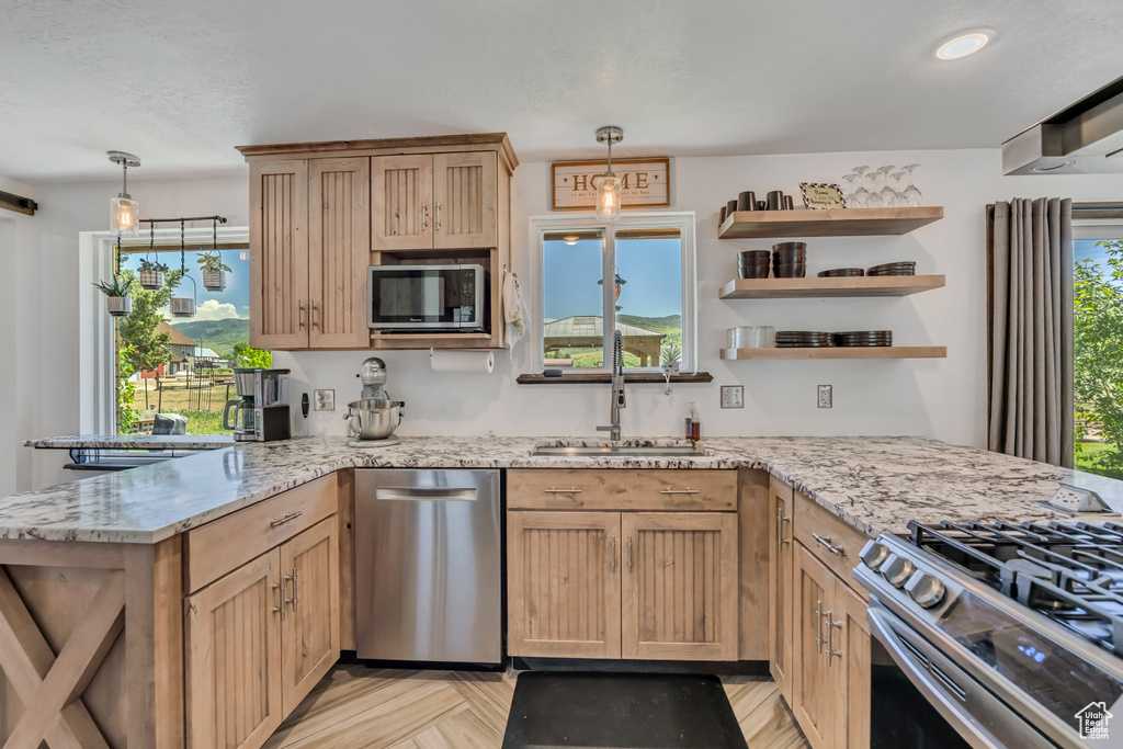 Kitchen with stainless steel appliances, a peninsula, decorative light fixtures, and light stone counters