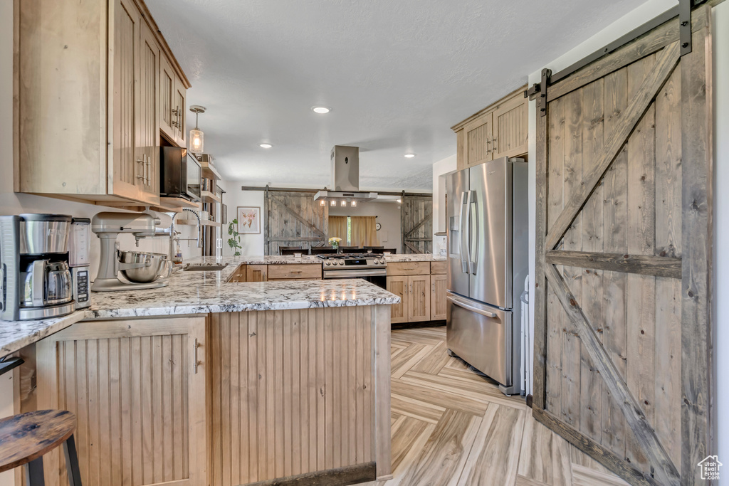 Kitchen featuring a barn door, appliances with stainless steel finishes, a peninsula, light brown cabinets, and island exhaust hood