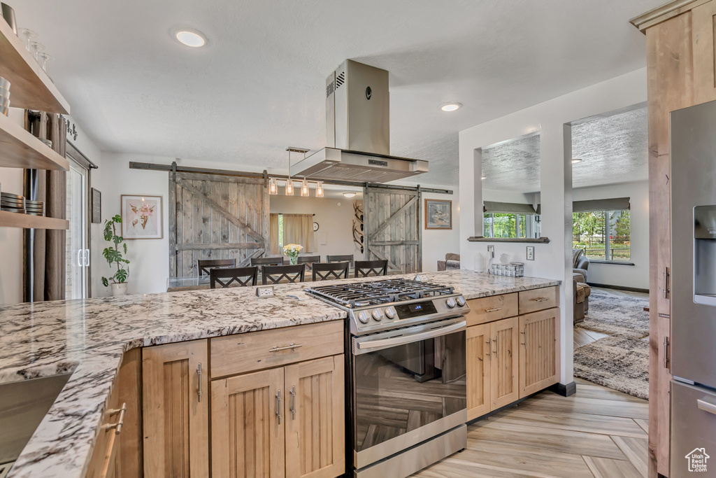 Kitchen with stainless steel appliances, island exhaust hood, light brown cabinets, a barn door, and recessed lighting