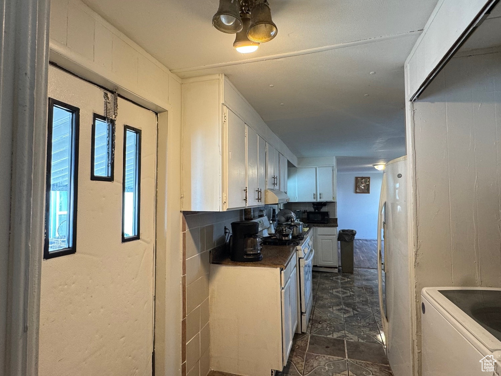 Kitchen featuring white cabinets, white gas stove, under cabinet range hood, separate washer and dryer, and dark countertops