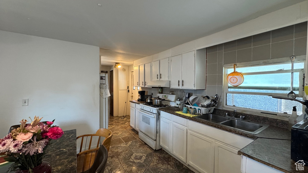 Kitchen featuring white gas range, a sink, under cabinet range hood, dark countertops, and white cabinets
