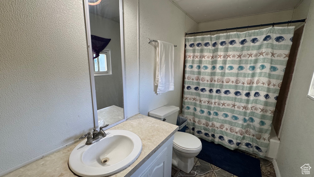 Full bathroom featuring a textured wall, toilet, vanity, and shower / tub combo with curtain