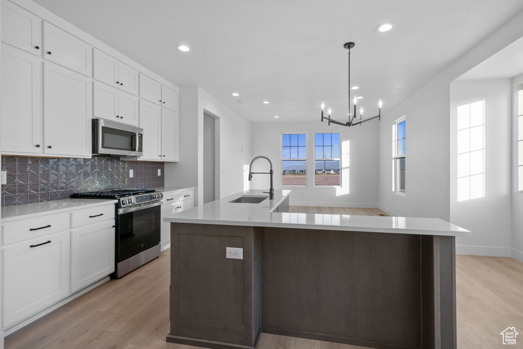 Kitchen with appliances with stainless steel finishes, light wood-style flooring, decorative backsplash, white cabinets, and recessed lighting