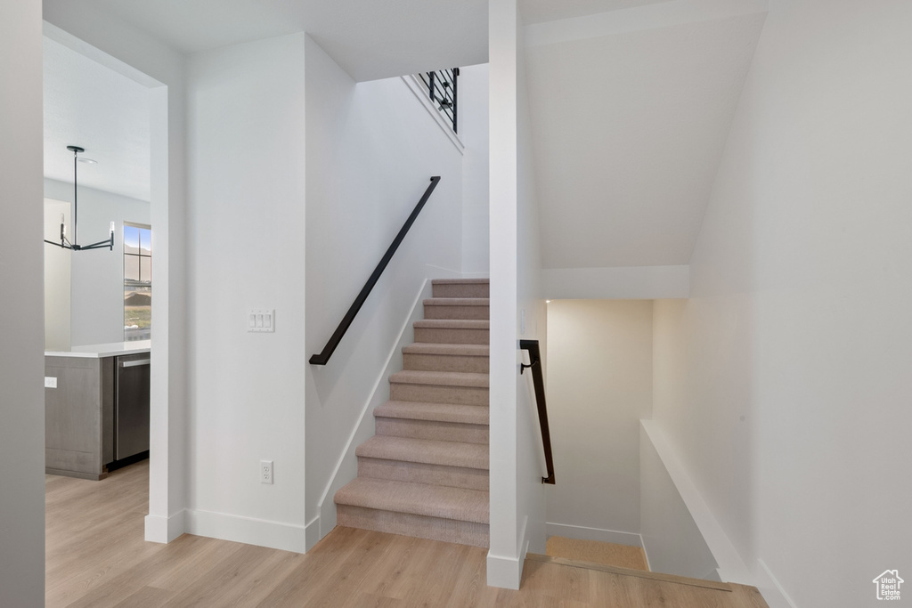 Stairs with wood finished floors and a chandelier