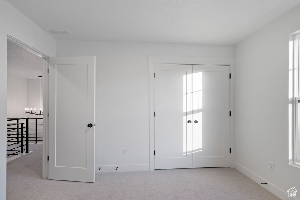 Unfurnished bedroom with carpet, a chandelier, multiple windows, and a closet