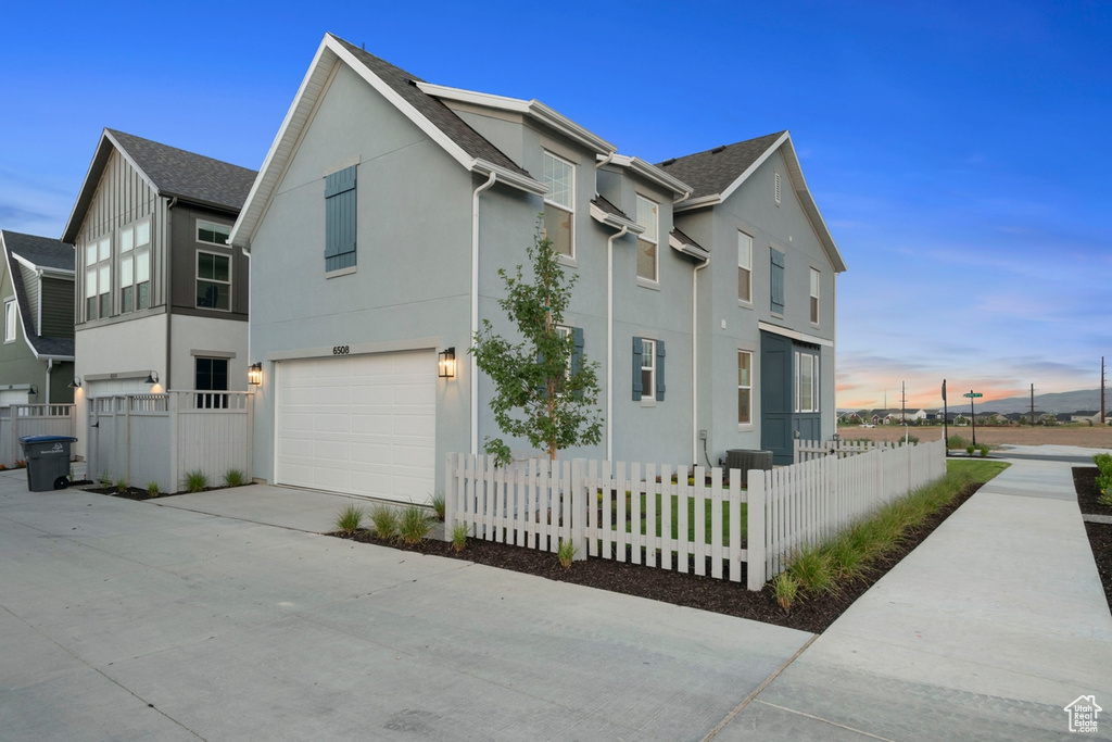 View of side of property featuring an attached garage, concrete driveway, stucco siding, and a fenced front yard
