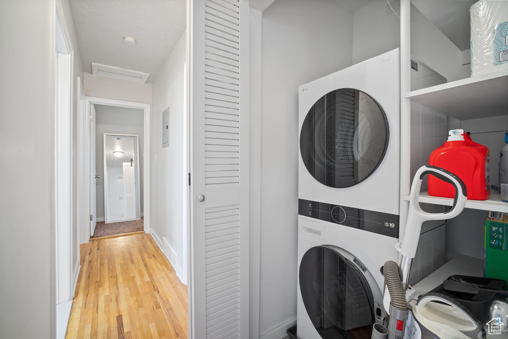 Laundry room with stacked washer and clothes dryer, attic access, and light wood-type flooring