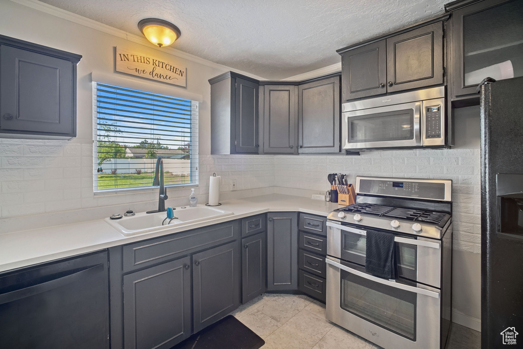 Kitchen featuring appliances with stainless steel finishes, a sink, tasteful backsplash, light countertops, and crown molding