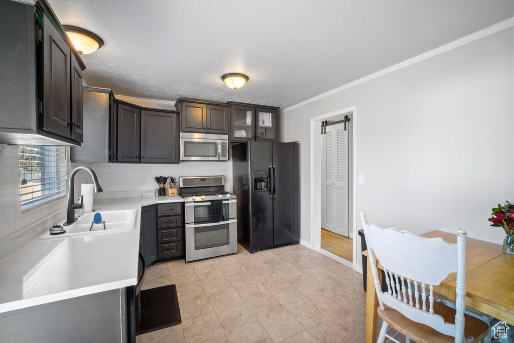 Kitchen featuring appliances with stainless steel finishes, a sink, light countertops, tasteful backsplash, and crown molding