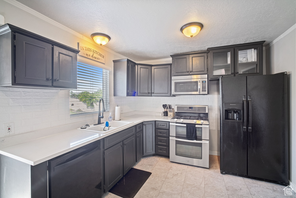 Kitchen with appliances with stainless steel finishes, a sink, ornamental molding, decorative backsplash, and light countertops