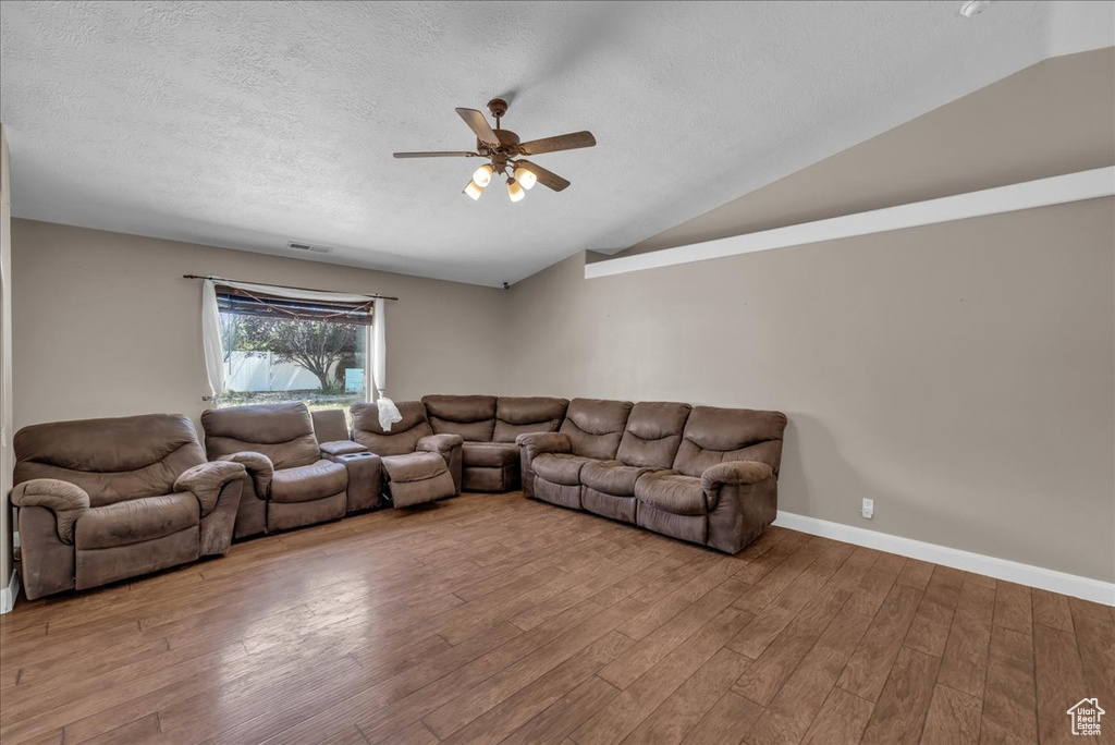 Living room with lofted ceiling, ceiling fan, wood finished floors, and a textured ceiling