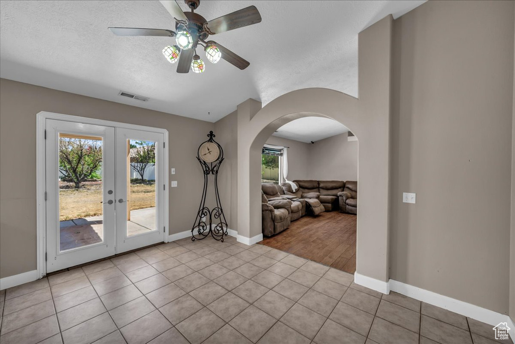 Tiled empty room with arched walkways, a ceiling fan, french doors, and lofted ceiling