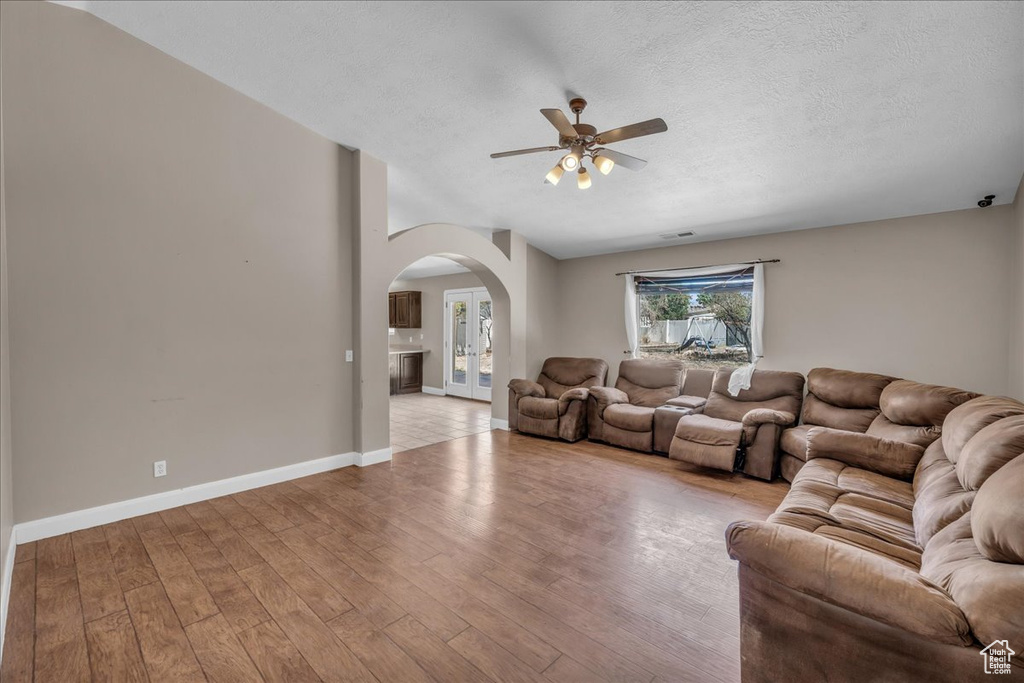 Living room featuring arched walkways, a ceiling fan, light wood finished floors, and a textured ceiling