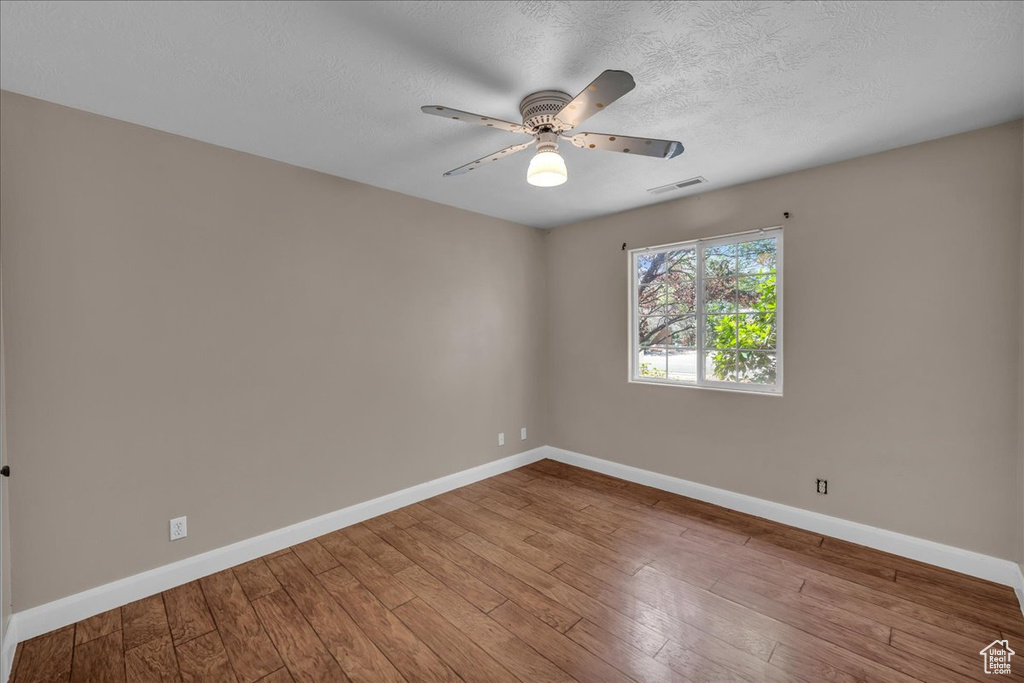 Empty room with ceiling fan, hardwood / wood-style flooring, and a textured ceiling