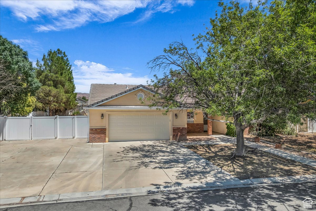 View of property hidden behind natural elements featuring brick siding, a gate, a garage, concrete driveway, and a tiled roof