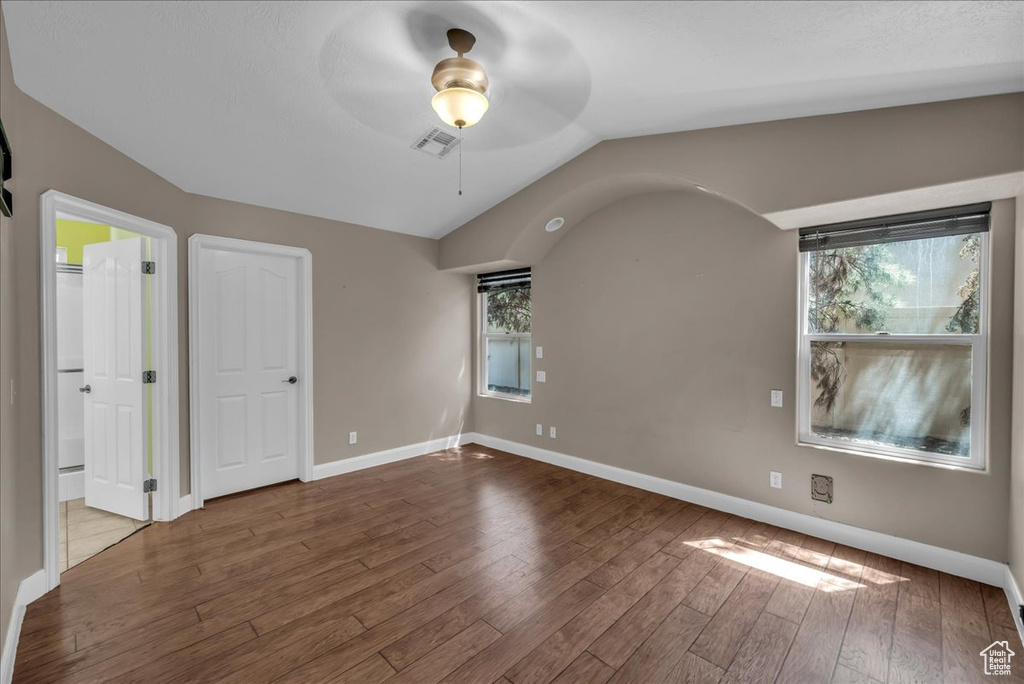 Unfurnished bedroom with wood finished floors, multiple windows, lofted ceiling, and ceiling fan