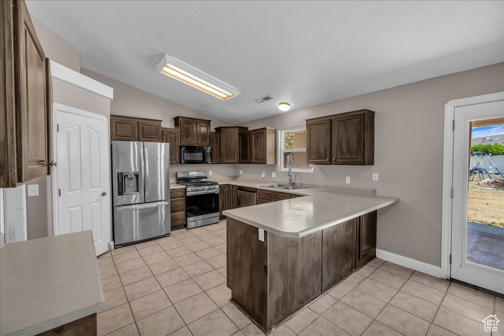 Kitchen with stainless steel appliances, a peninsula, vaulted ceiling, dark brown cabinetry, and light countertops